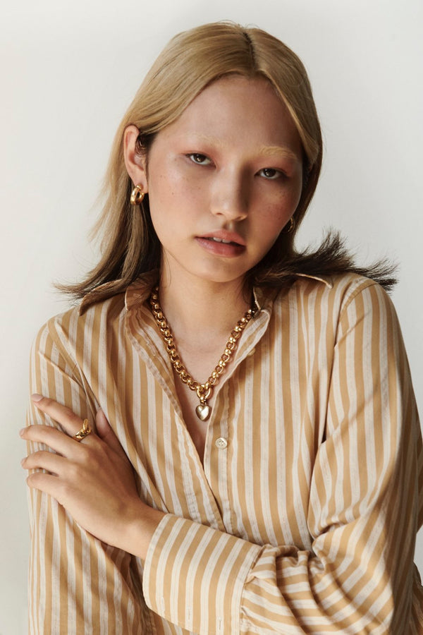 Model wearing Laura Lombardi gold Amorina heart charm pendant and Mini Icona hoop earrings.