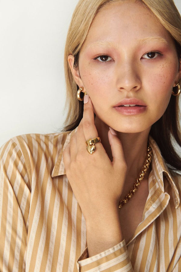 Model wearing gold Laura Lombardi Amorina heart charm ring and mini icona hoops.