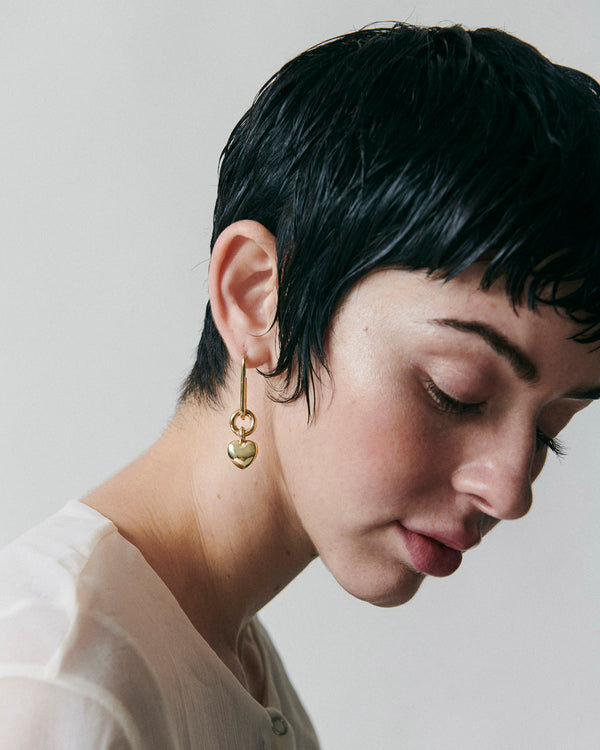 Model wearing Laura Lombardi gold Ilaria Earrings with small heart shaped drop detail.