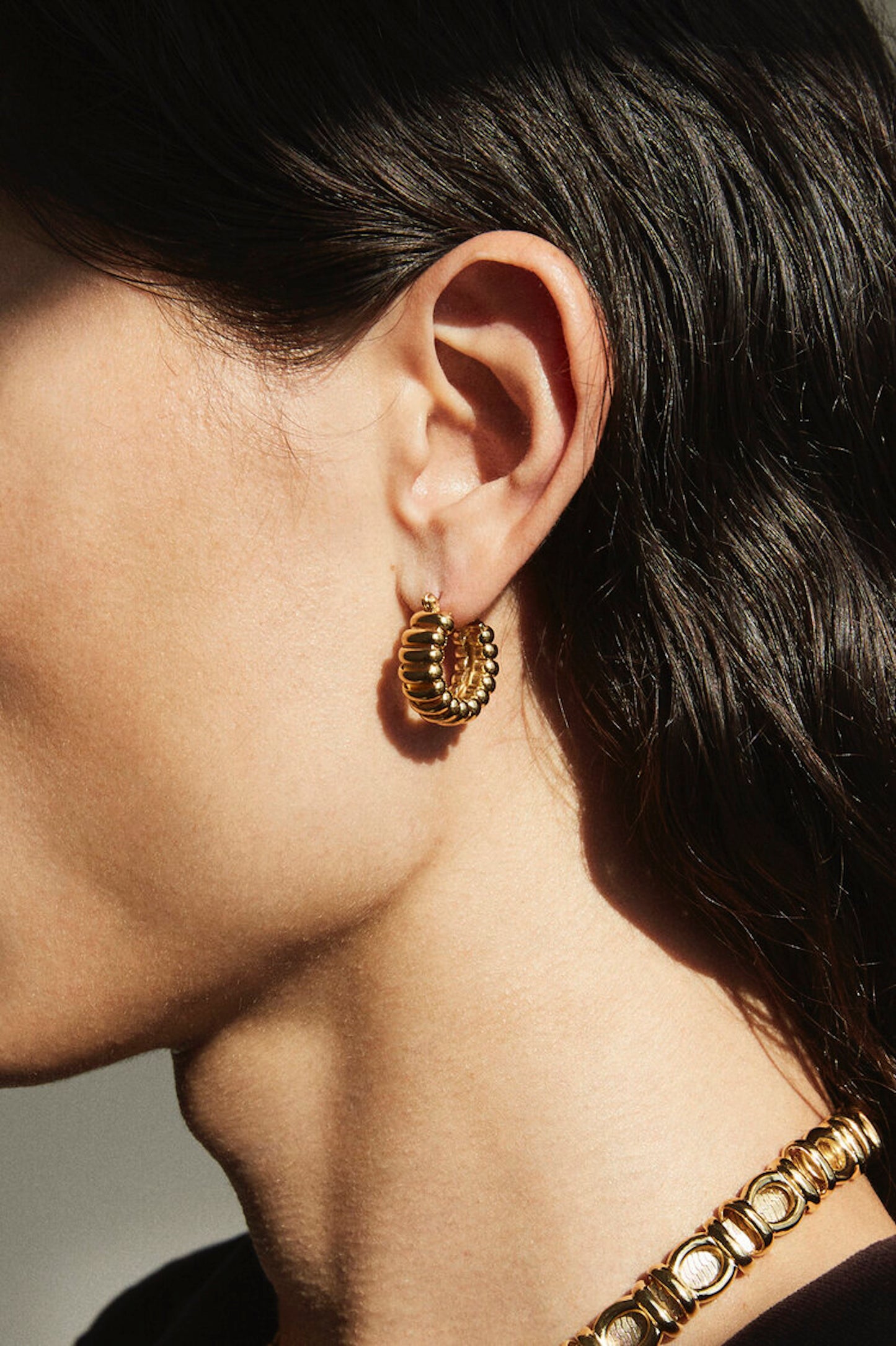 Side profile of model wearing Laura Lombardi gold Mini Camilla hoop earrings.