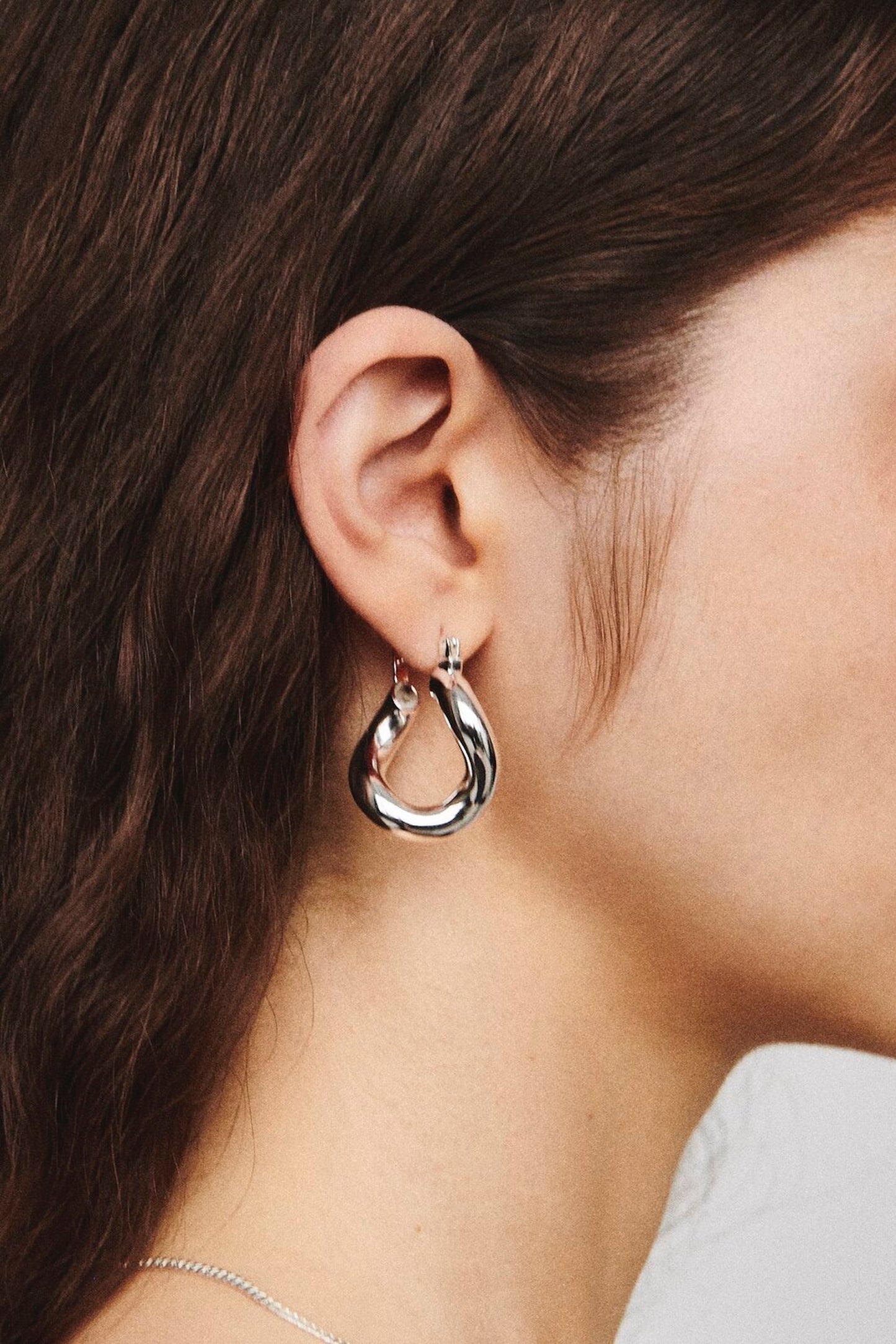 Side profile of model wearing Laura Lombardi silver sculptural Mini Anima hoop earrings.